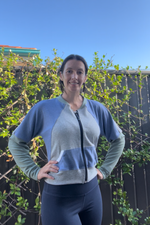Woman wearing a blue and grey zip-up athletic jacket with raglan dolman sleeves, kangaroo pocket, and curved waistband. Sewing pattern for jackets by Ellie and Mac sewing patterns. 