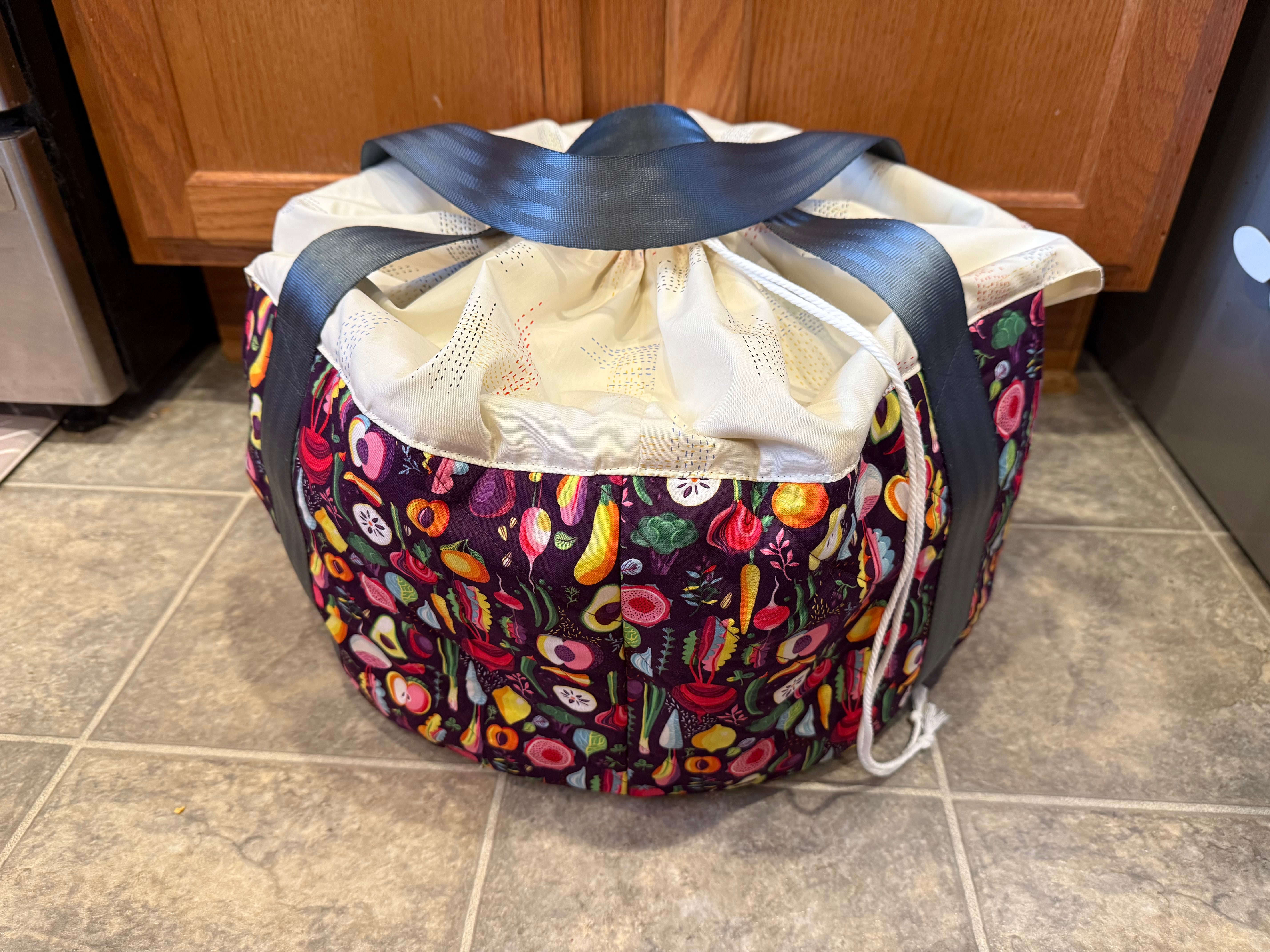 Colorful slow cooker insulated carrier bag with drawstring top on a tiled floor. Easy craft sewing patterns for the home. Makes great holiday and housewarming gifts!