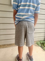 Person wearing a blue and white striped shirt and gray shorts standing against a beige wall. 