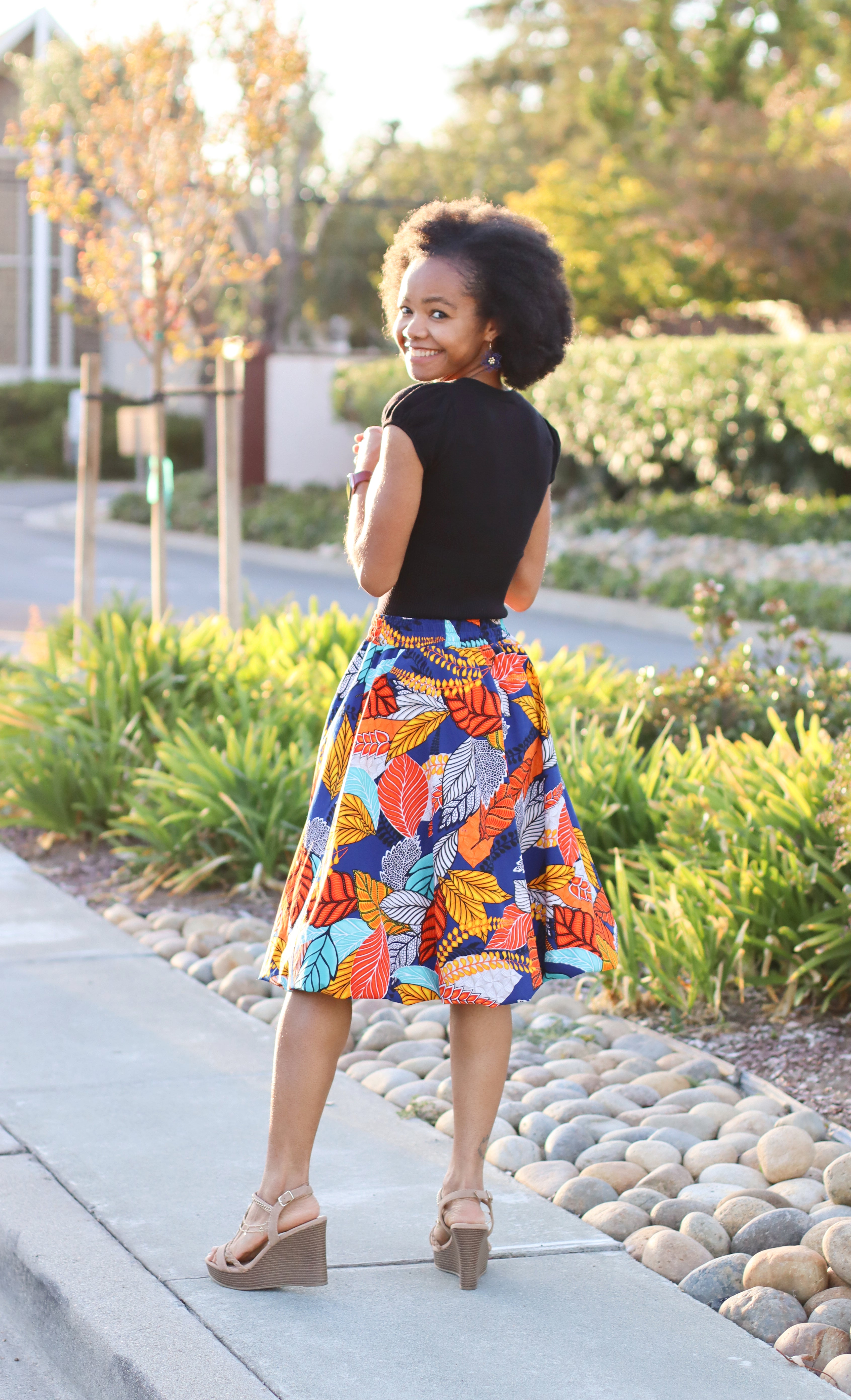 Woman in a colorful knee length woven skirt standing outdoors on a sunny day.