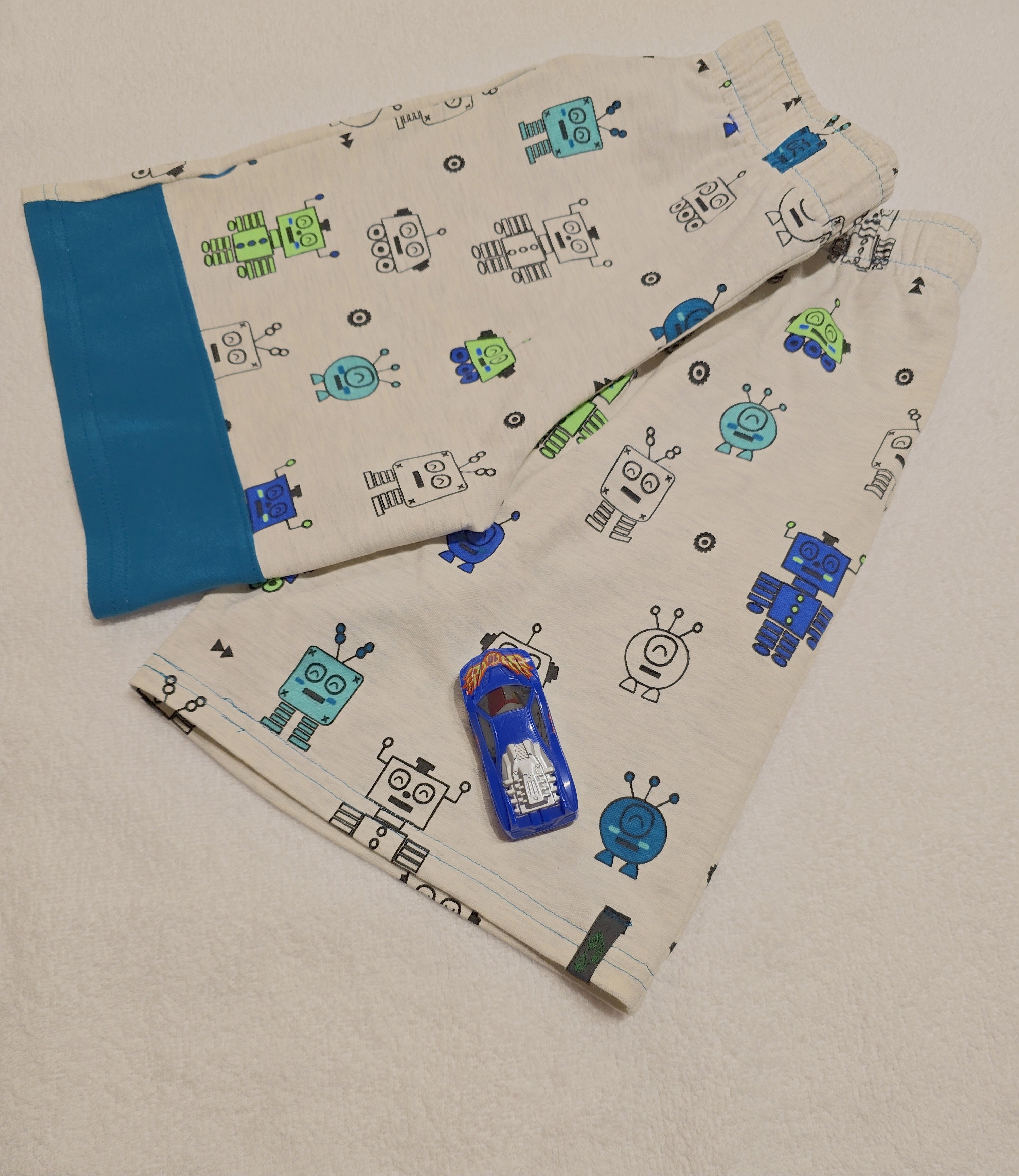 Knit fabric shorts with robot pattern on a beige background with teal color block section.