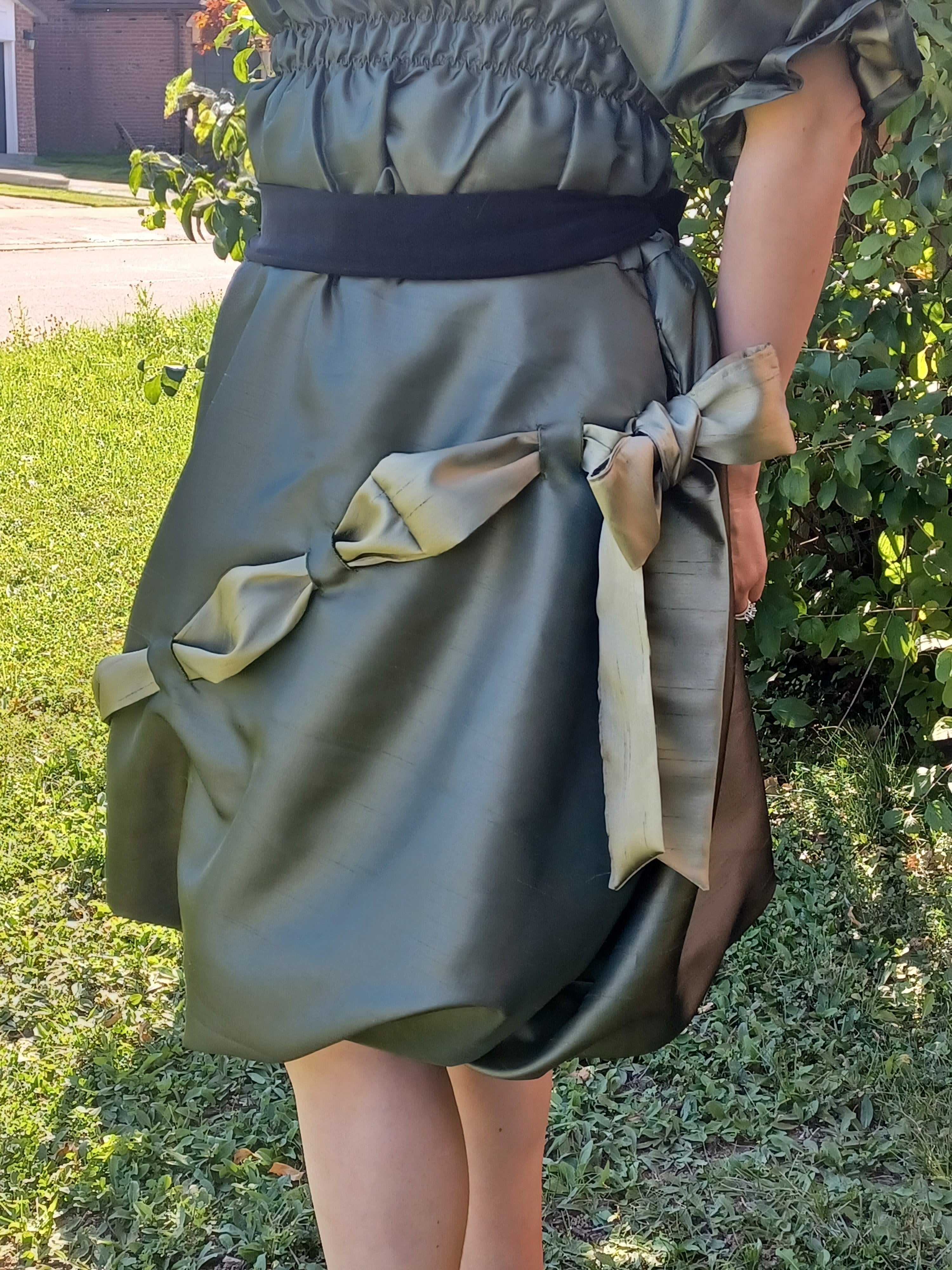 Person wearing a green bubble skirt with large bows outdoors on grass.