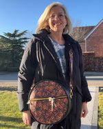 Woman holding a round bag with a geometric butterfly pattern outdoors on a clear day.