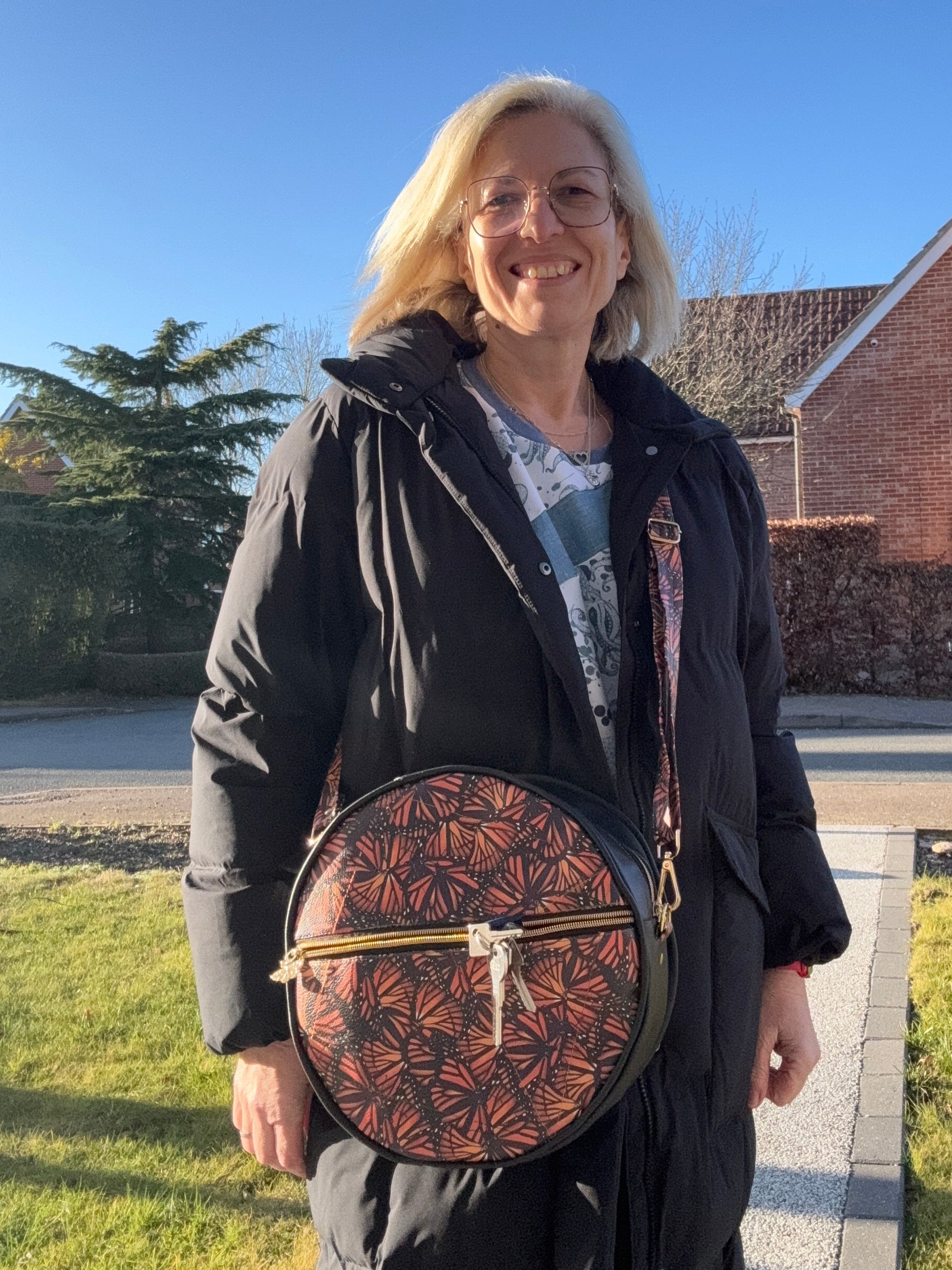 Woman holding a round bag with a geometric butterfly pattern outdoors on a clear day.