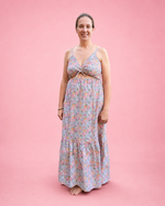 A woman modeling a sleeveless, floor-length floral maxi dress with a ruched front bodice to create an adjustable cutout, standing against a solid pink studio background. Dress made using Ellie and Mac PDF sewing patterns. Easy sewing patterns for beginners. Includes A4, Letter, A0, and projector files. Sew along video included.