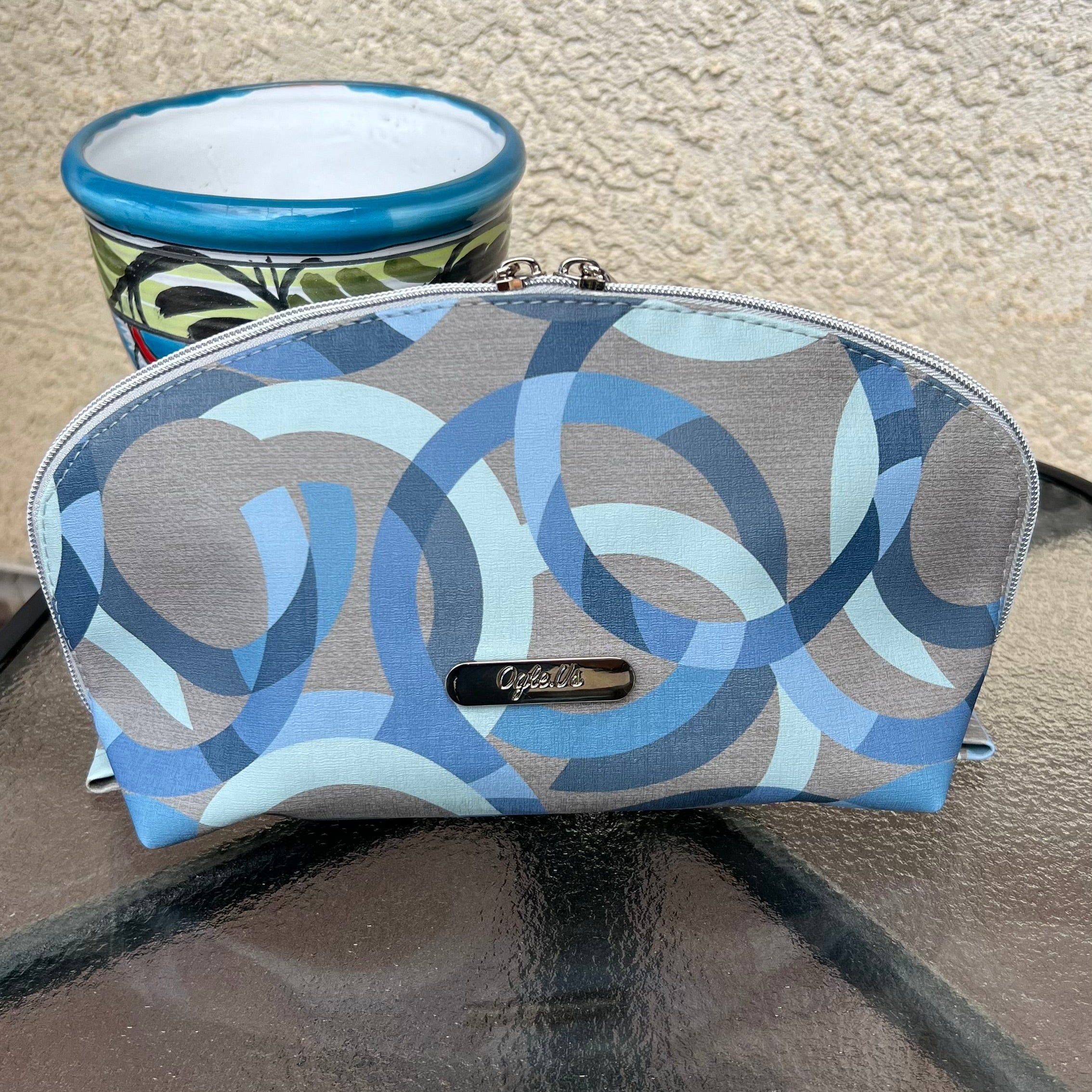 Patterned Tessa cosmetic bag on a glass table with a textured wall background. 