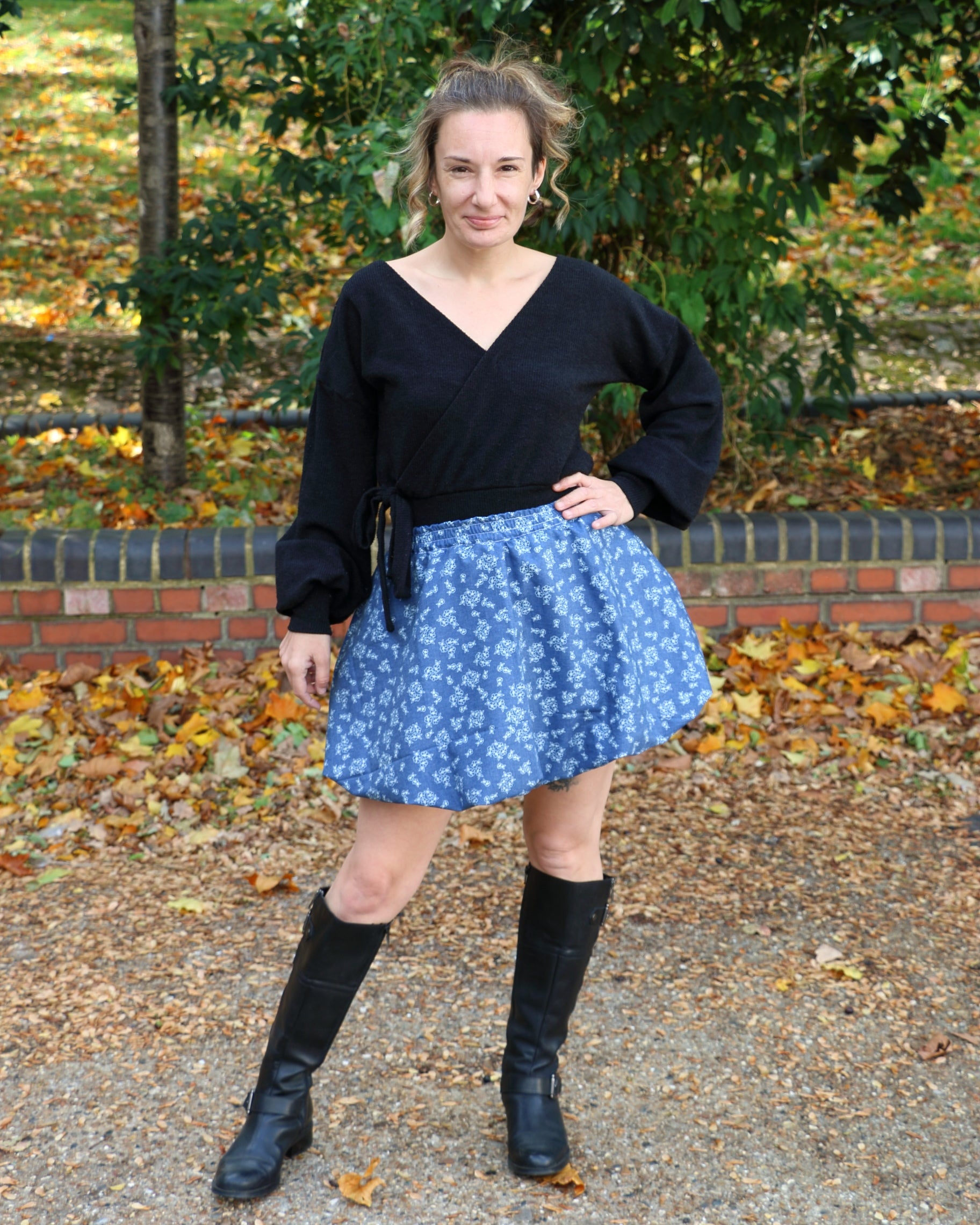 Woman wearing a black top and blue patterned mini bubble skirt standing outdoors with fallen leaves on the ground.