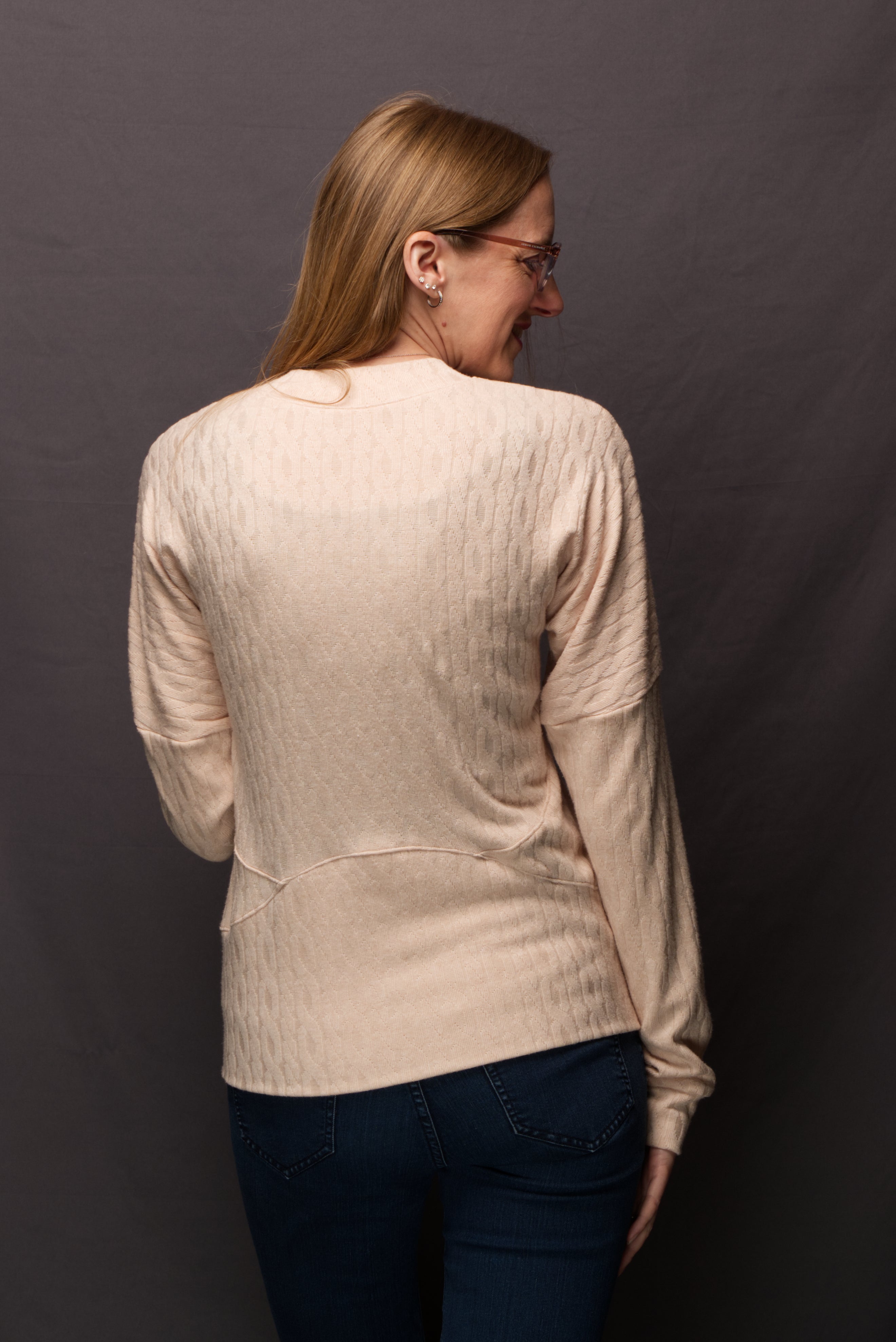 Woman wearing a sweater knit fabric zip-up jacket with raglan dolman sleeves, kangaroo pocket, and curved waistband. Knit fabric sewing pattern - instant download. High Hip Version.