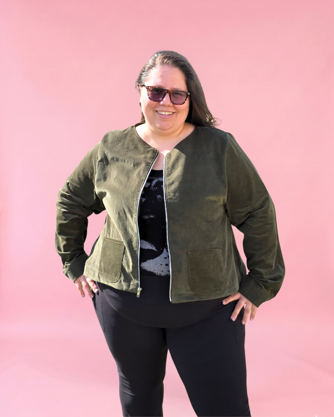 Person wearing a green jacket with zip and pockets and sunglasses against a pink background. Plus size sewing patterns xxs - 6xl size range. 