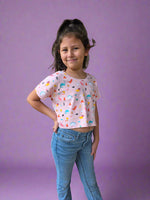 Young girl standing on a brick pavement wearing a patterned crop top and jeans.