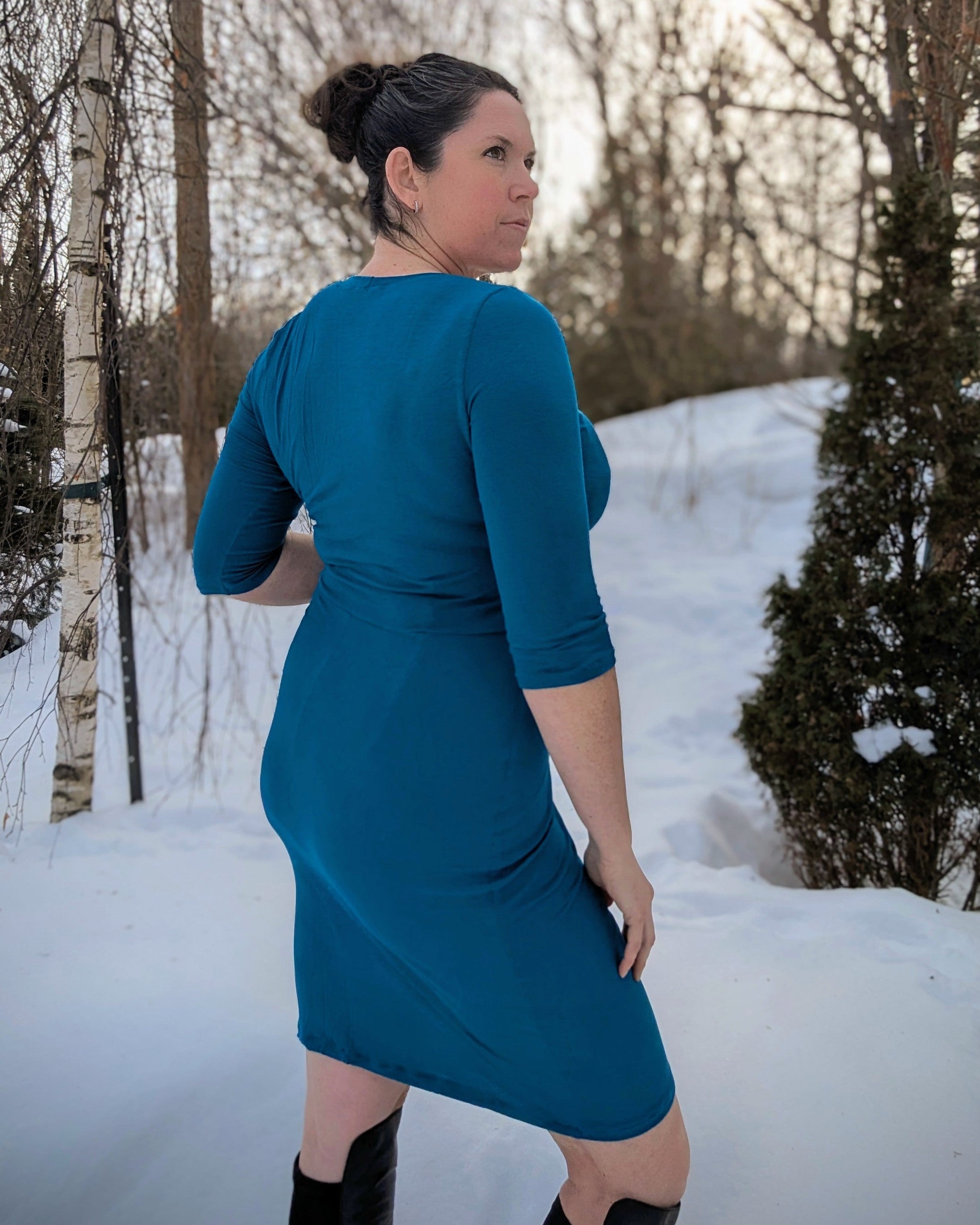 Woman in a teal dress standing in a snowy landscape with bare trees.