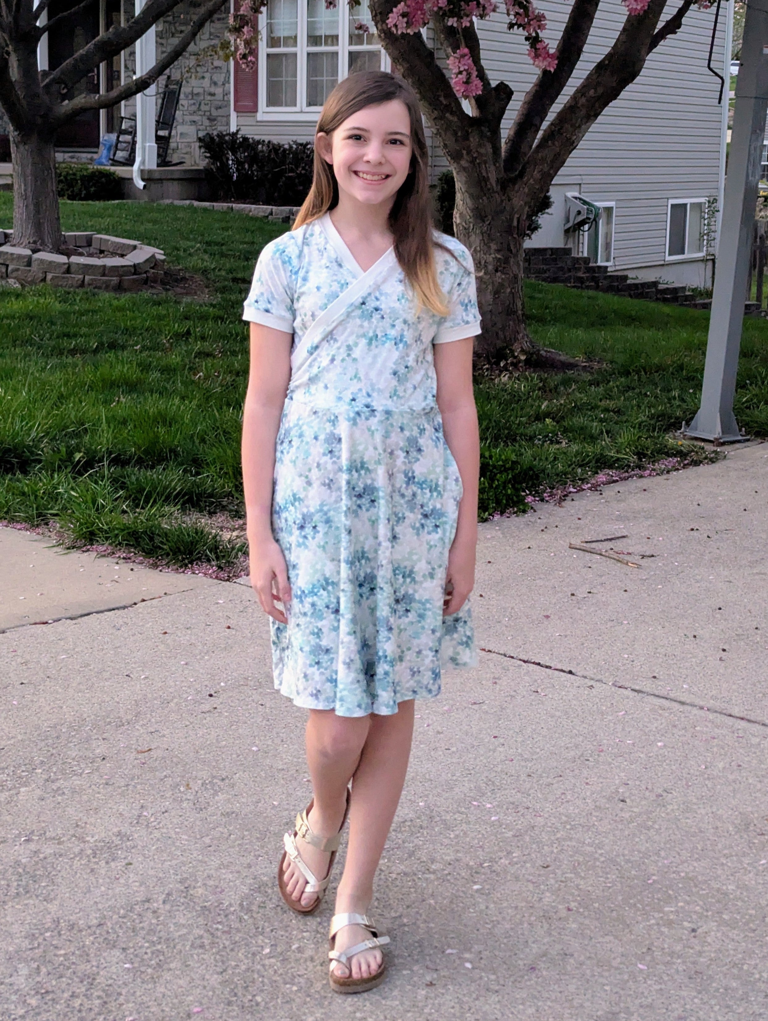 Floral fabric dress with faux wrap bodice and short sleeves. 1/2 Circle skirt with pockets. Toddler to teen sewing pattern.