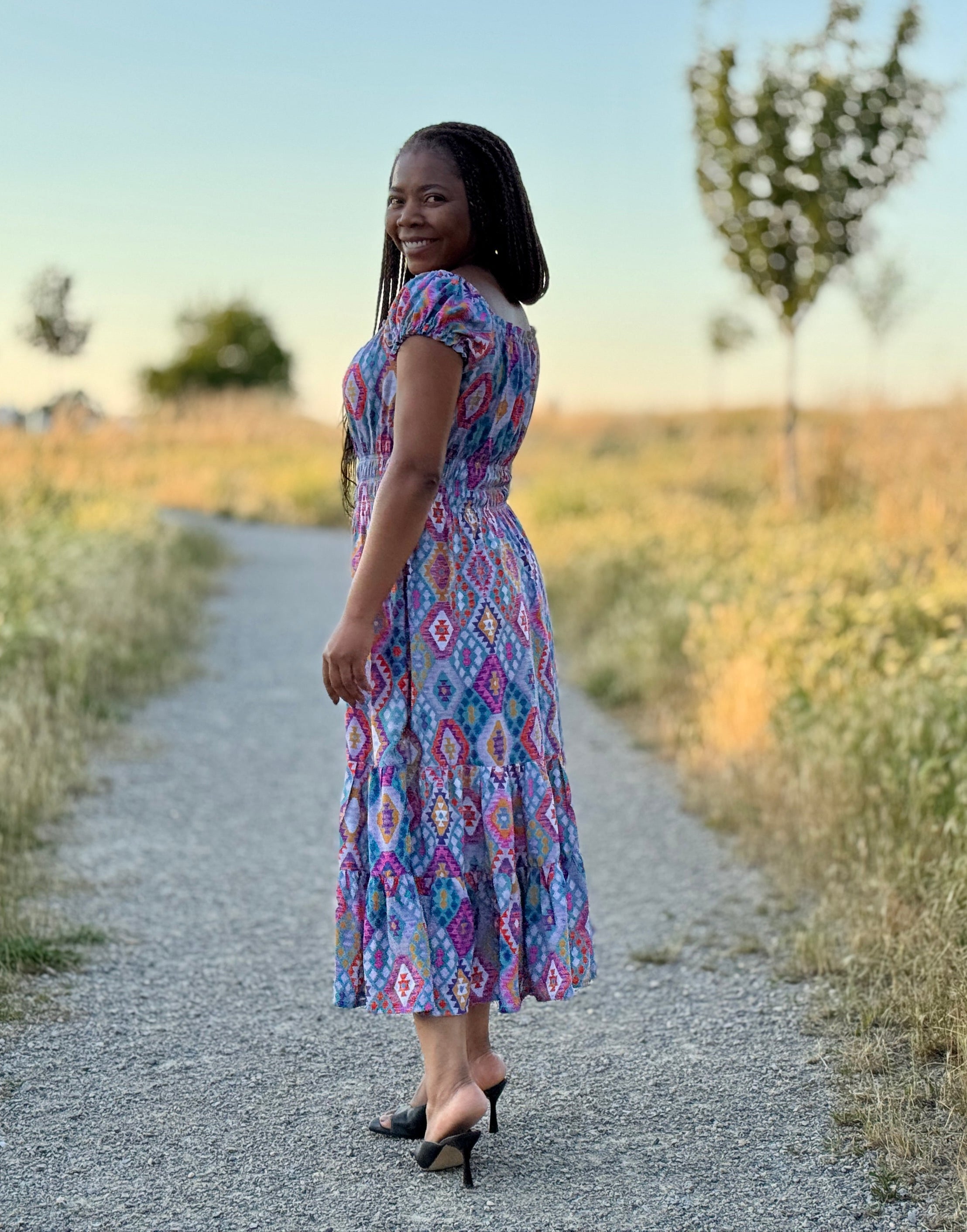 Woman in a floral dress walking on a path through a field with trees in the background. The dress was made using the PDF sewing pattern by Ellie and Mac.