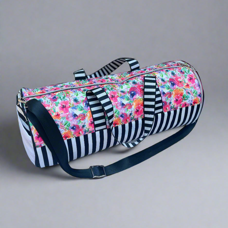 Serena Sports Duffle Bag in a waterproof floral canvas fabric and white and black contrasting bottom panel. Adjustable shoulder straps and hand straps. Side Zipper shoe compartment to keep dirty shoes away from clean clothes. Side mesh pocket for quick access to keys, phone, airpods, and more. Easy PDF sewing pattern by Ellie and Mac Sewing Patterns.