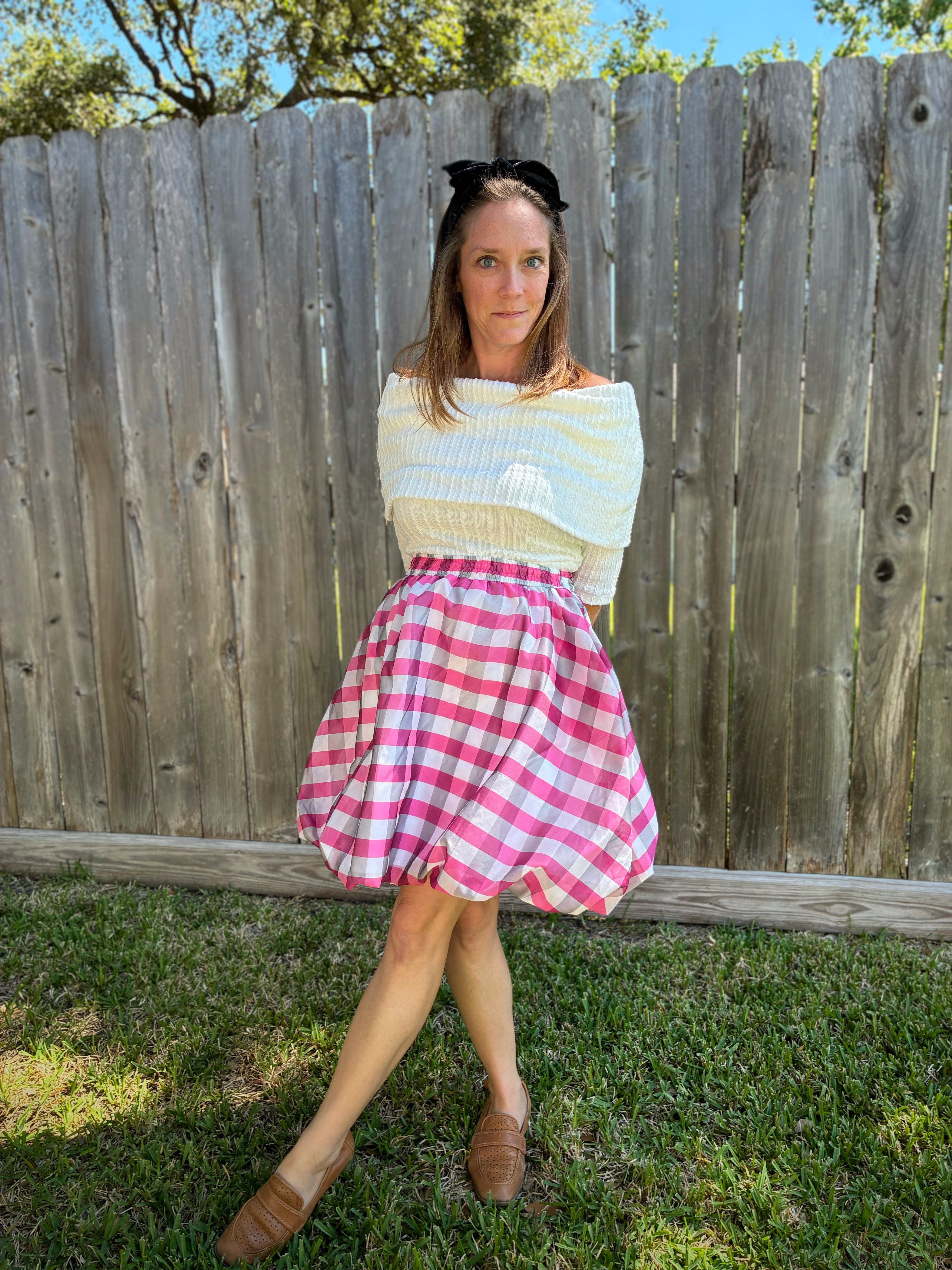 Woman wearing a sweater and checkered skirt standing in front of a wooden fence. This entire outfit was made using Ellie and Mac's Beginner Friendly sewing patterns. 