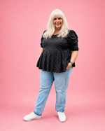 A woman with long white hair stands against a solid pink studio background wearing a black puff-sleeve top with white polka dots, light blue jeans, and white sneakers. The top is made using Ellie and Mac PDF sewing patterns. They include A4, Letter, A0, and Projector pattern files. They also include a full sew-along tutorial. 