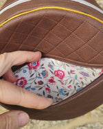 Close-up of a brown leather product with floral interior, held by a hand on a natural stone background.