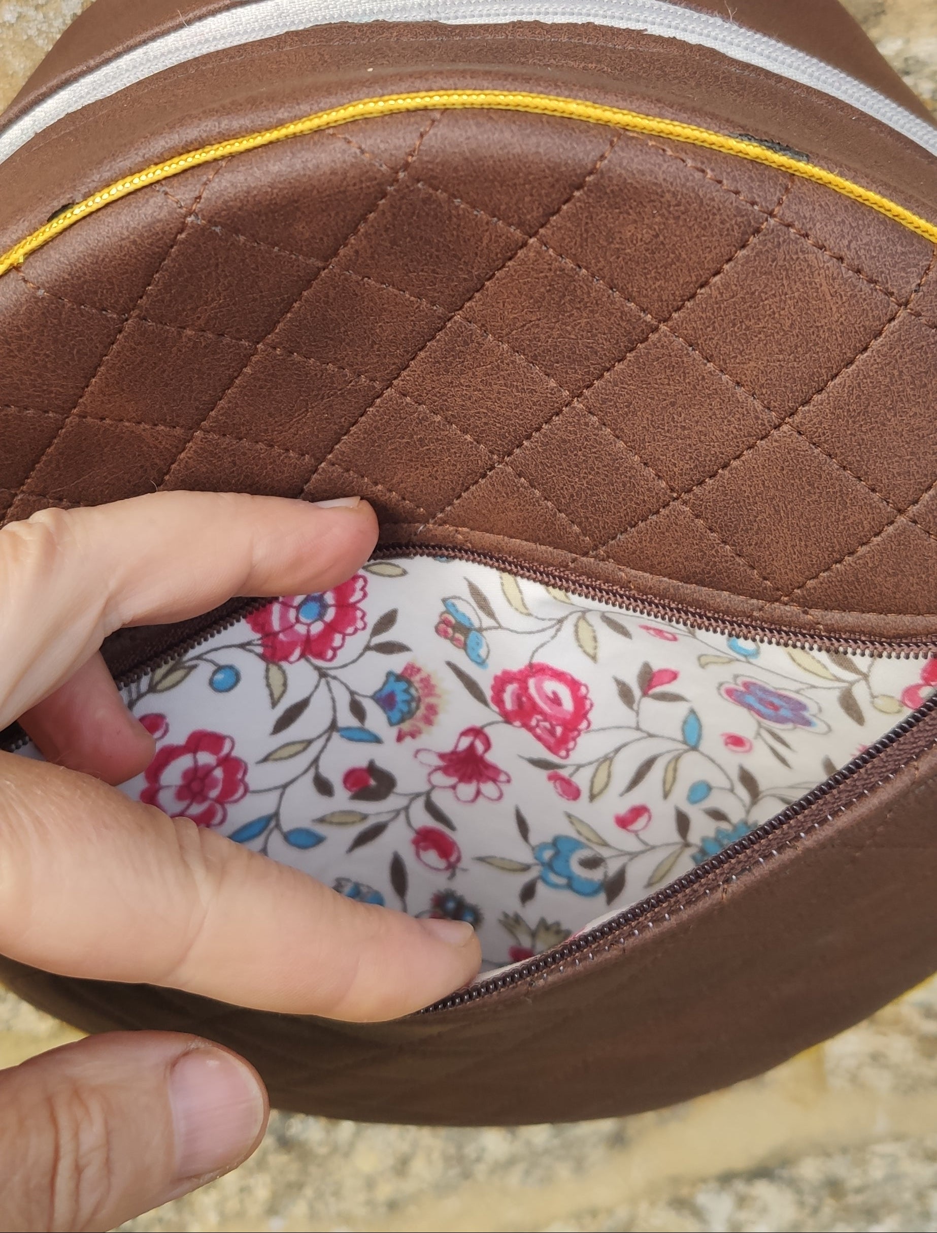 Close-up of a brown leather product with floral interior, held by a hand on a natural stone background.