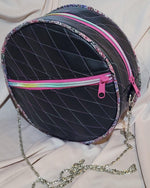 Round black bag with colorful zippers and a chain strap on a light pink fabric background