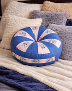 Decorative round pillow with floral patterns on a bed with fluffy pillows and a blanket.