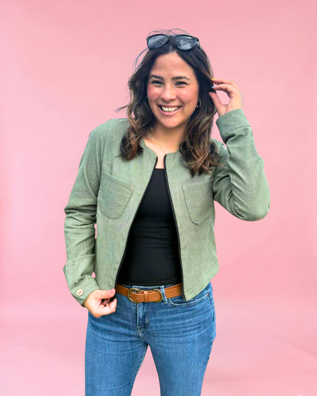 Woman wearing a green linen jacket, black top, and blue jeans against a pink background. Stylish sewing patterns.