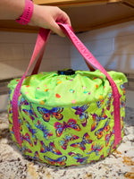 Green slow cooker carrier with butterfly pattern with hot pink straps, held by a hand on a kitchen counter. Made using the Ellie and Mac Warm and Cozy Slow Cooker Carrier Pattern.