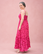 A woman modeling a bright pink sleeveless maxi dress with a dark pink floral pattern, standing against a solid dusty pink studio backdrop.