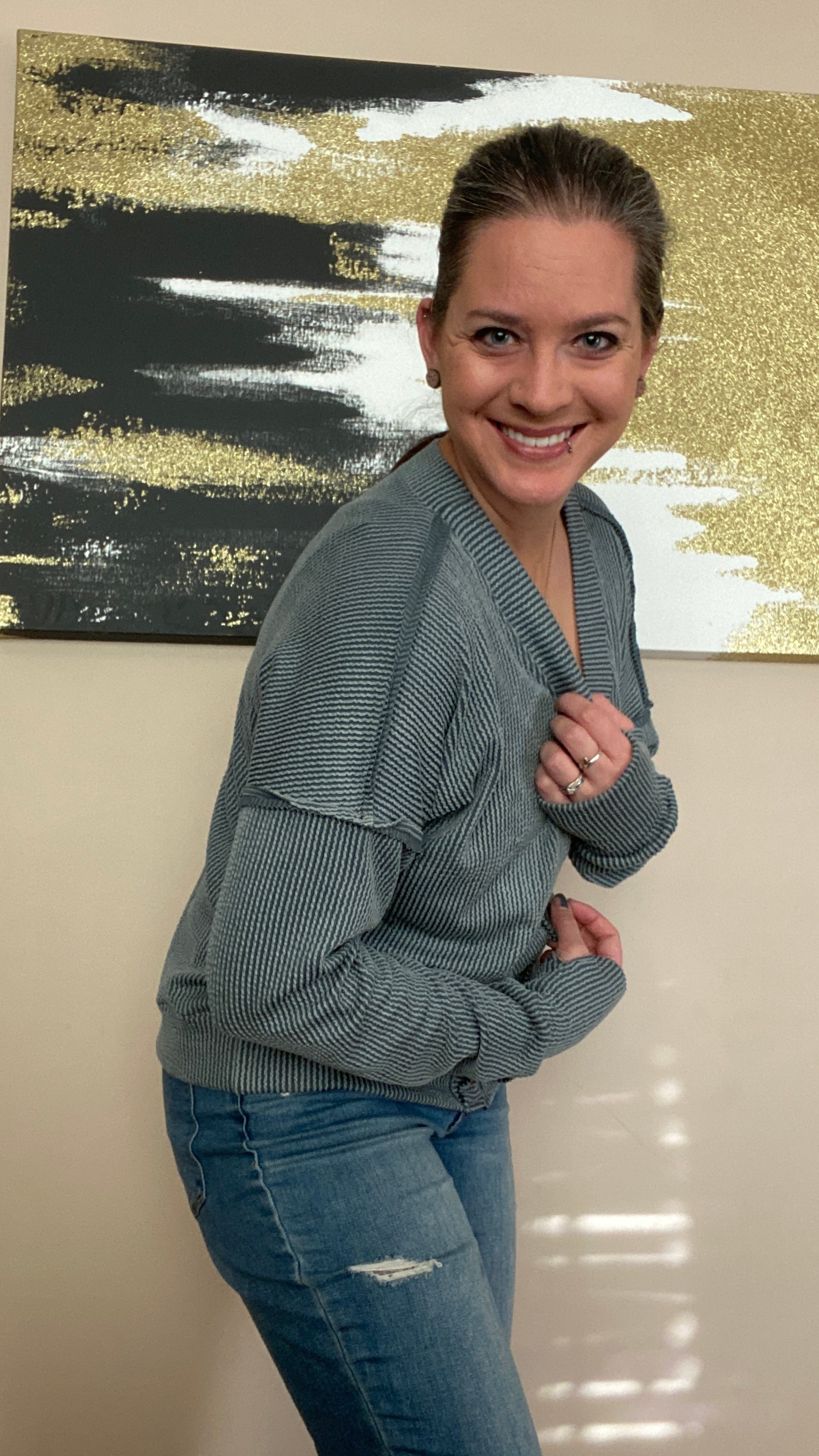 Woman wearing a gray cardigan sweater and blue jeans standing in front of abstract art on a wall.