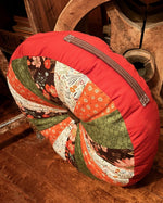 Decorative pillow with a patchwork design on a wooden floor with a large wooden wheel in the background. Made using the Sydney Sprocket Pillow Sewing Pattern.