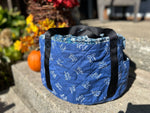 Blue quilted slow cooker bag with black straps on a stone surface with outdoor background. Great for gift making, tailgating, parties, potlucks, holiday gatherings, and more.