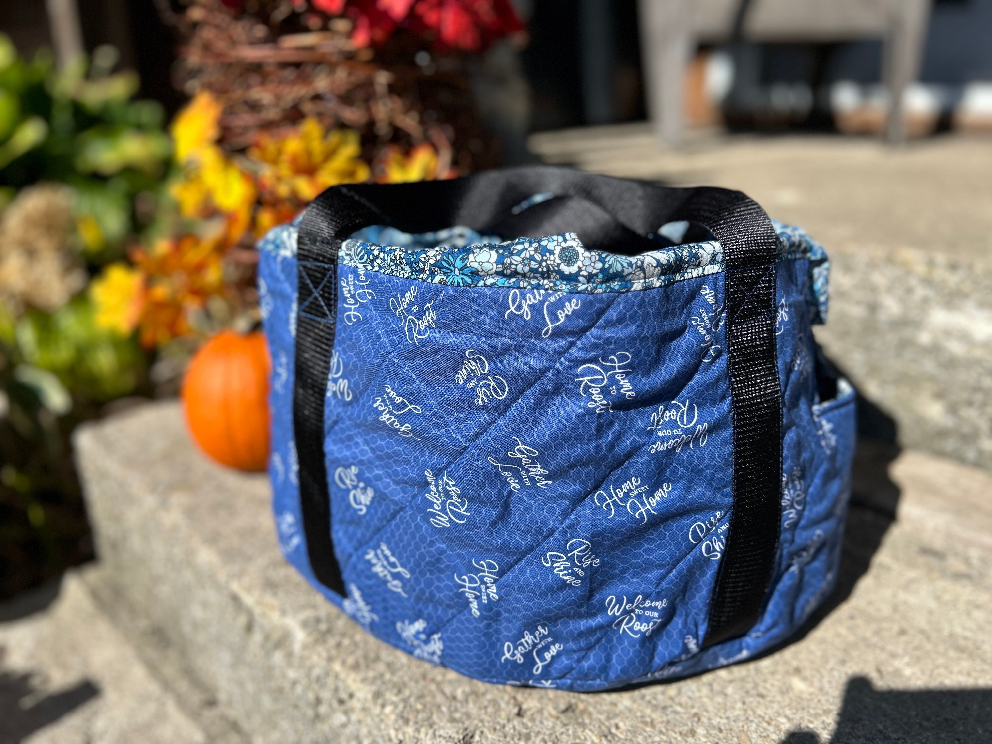 Blue quilted slow cooker bag with black straps on a stone surface with outdoor background. Great for gift making, tailgating, parties, potlucks, holiday gatherings, and more.