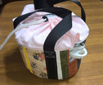 Fabric slow cooker carrier with floral pattern and black straps on a wooden surface.