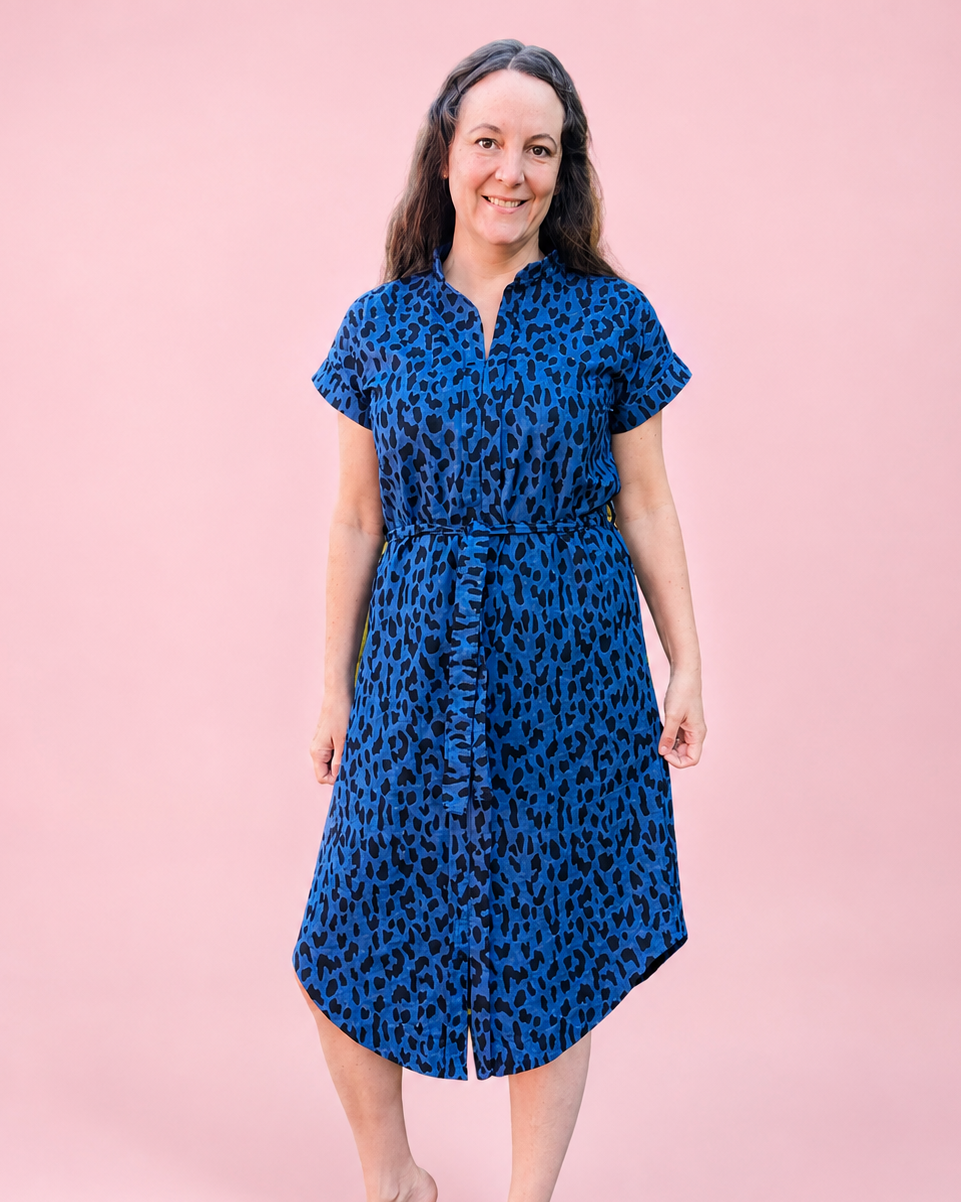 A woman modeling a short-sleeve blue and black leopard-print midi dress with a sash standing against a solid pink studio background. Dress made using Ellie and Mac PDF sewing patterns. They include A0, A4, Letter, print files and projector sewing file. They also include a full sew along video tutorial.