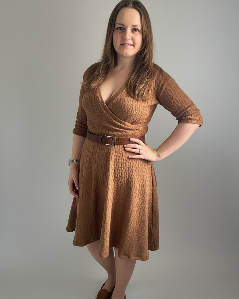 Woman wearing a brown dress standing against a white wall.