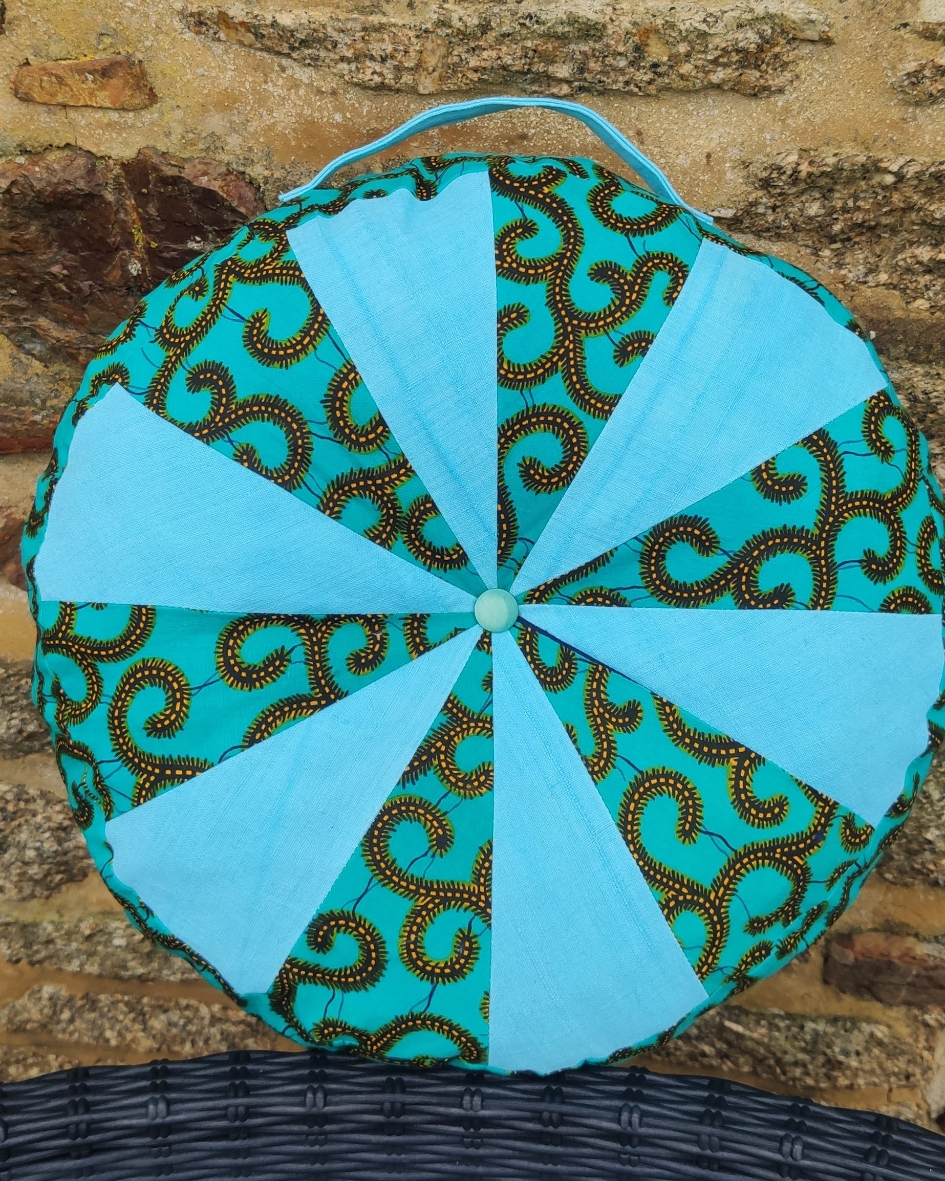 Turquoise fabric patchwork pillow with brown pattern on a stone surface