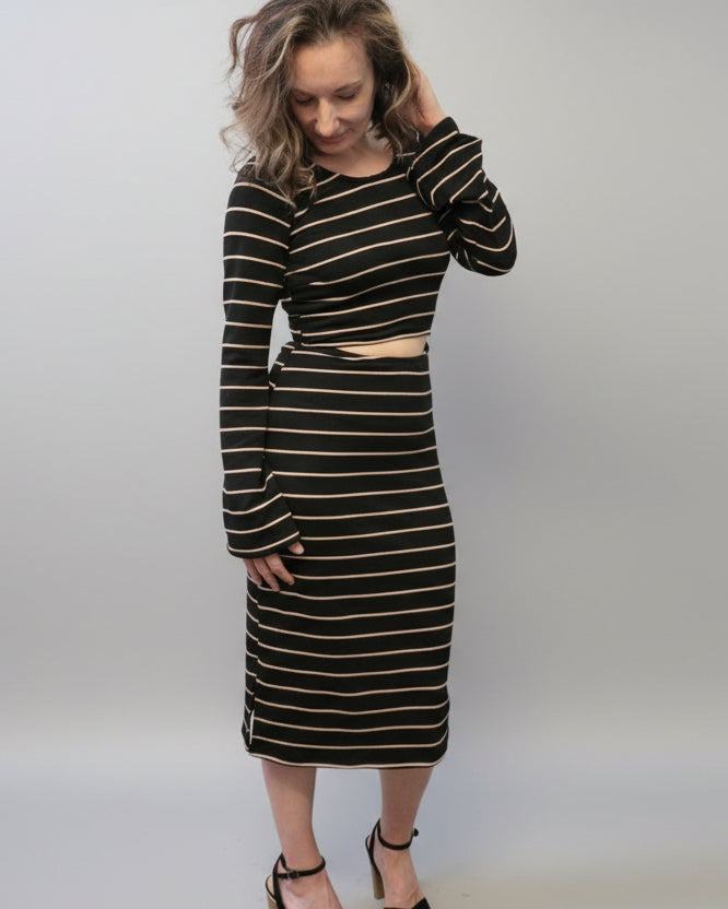 Woman wearing a black and gold striped dress against a white wall. Bell sleeve and front and back cutouts make this dress a must-have. PDF sewing pattern