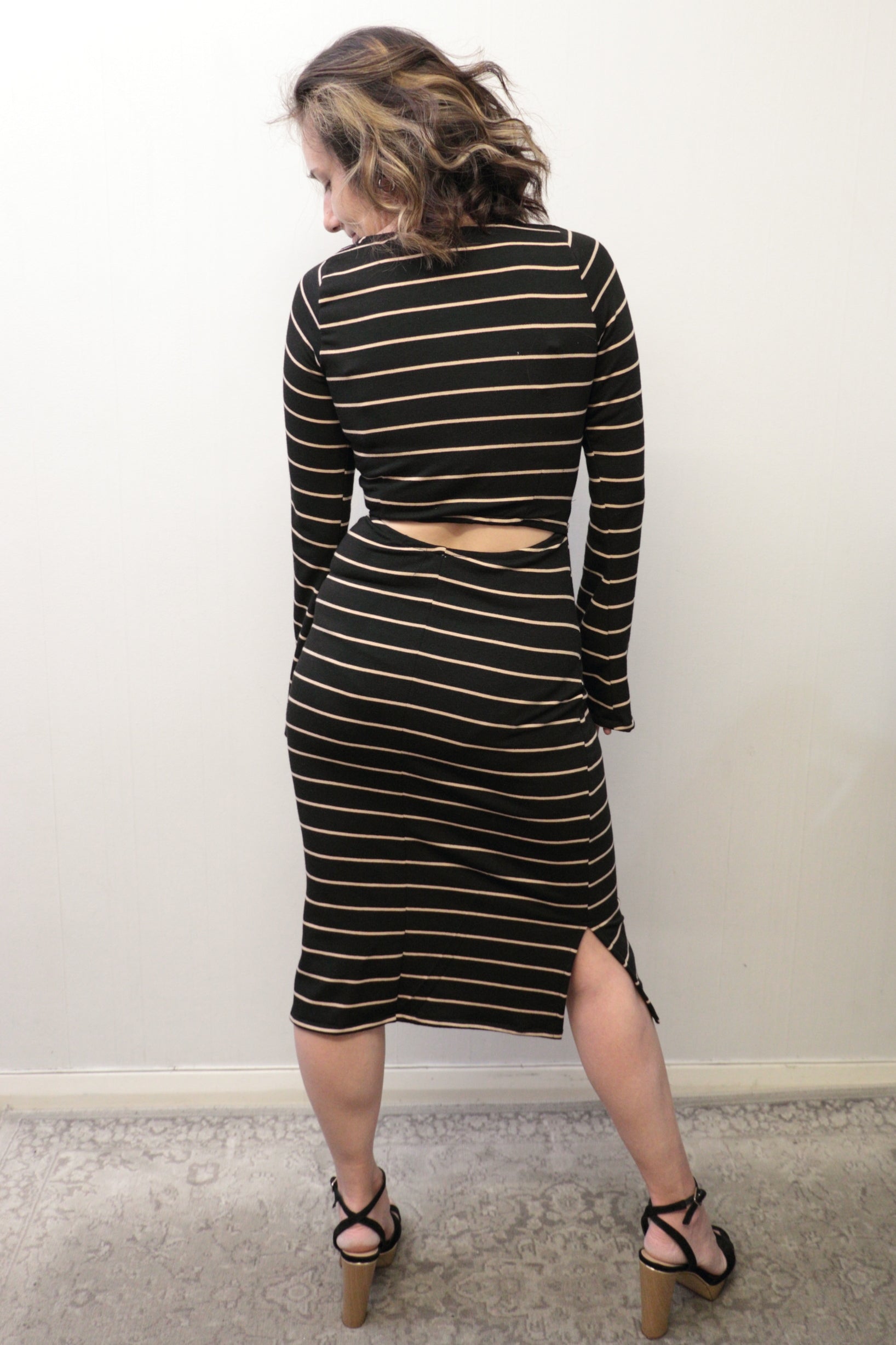 Woman wearing a black and gold striped dress with cut-out design, standing against a white wall.