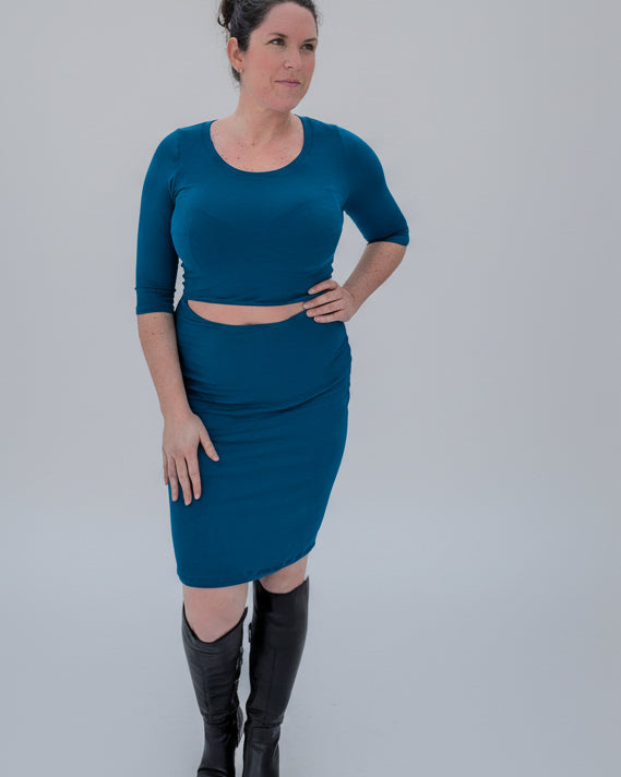 Woman in a teal fitted dress with front cutout standing in a snowy landscape with trees.