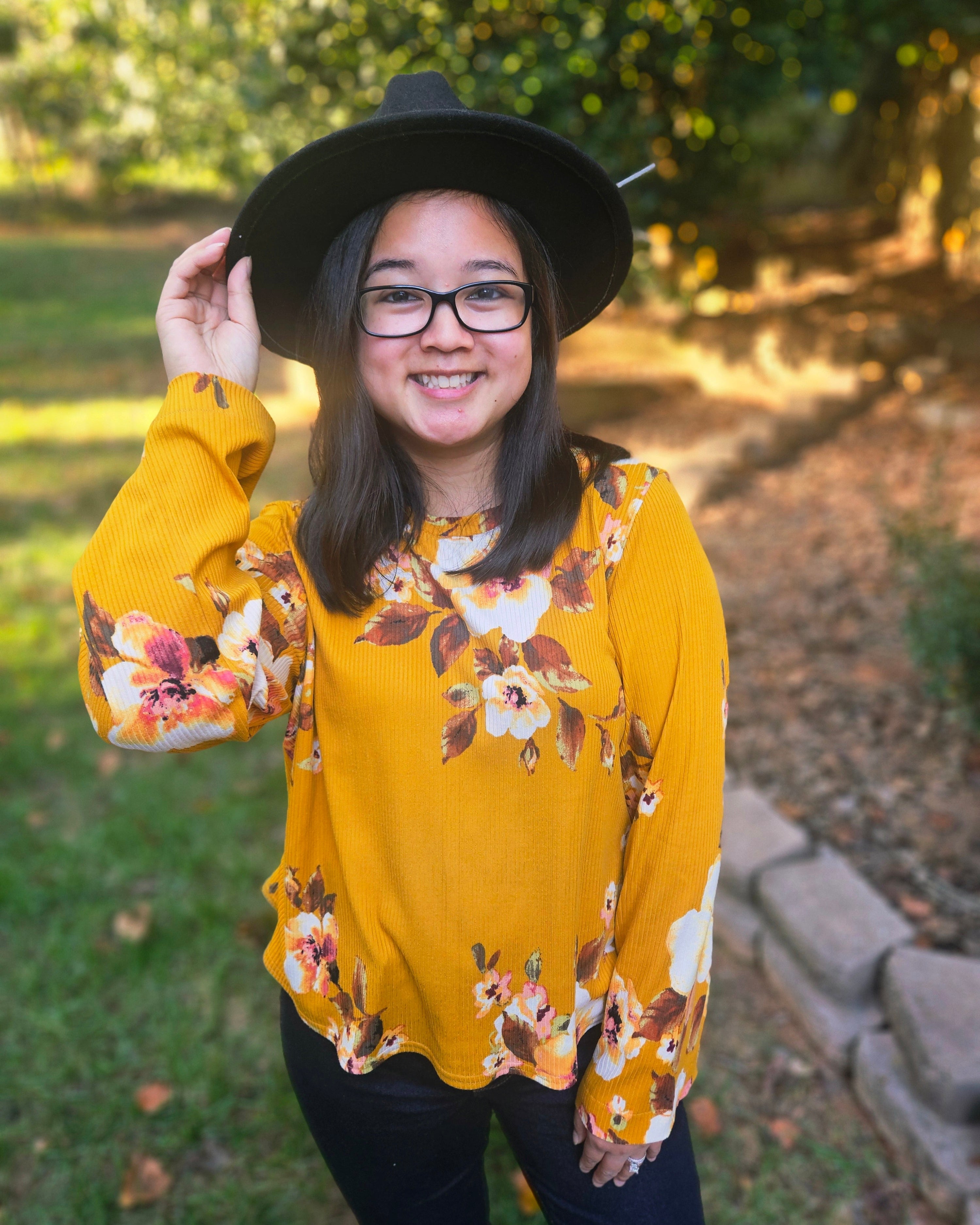 Person wearing a yellow floral sweater and black hat outdoors. Sew your own clothes with Ellie & Mac patterns. Size inclusive.