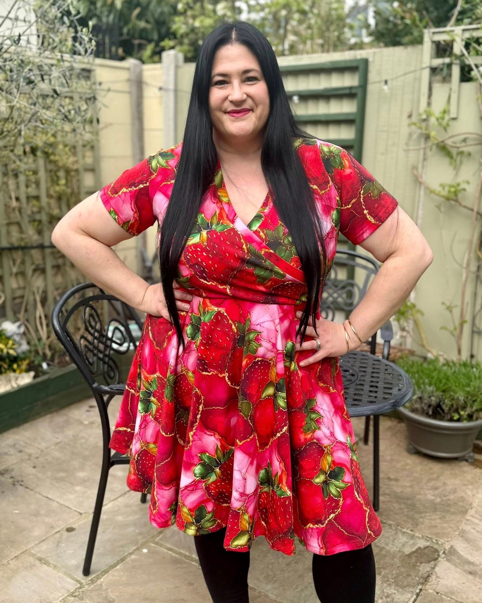 Woman wearing a red floral dress made using Ellie and Mac Sewing Patterns standing outdoors in a garden.
