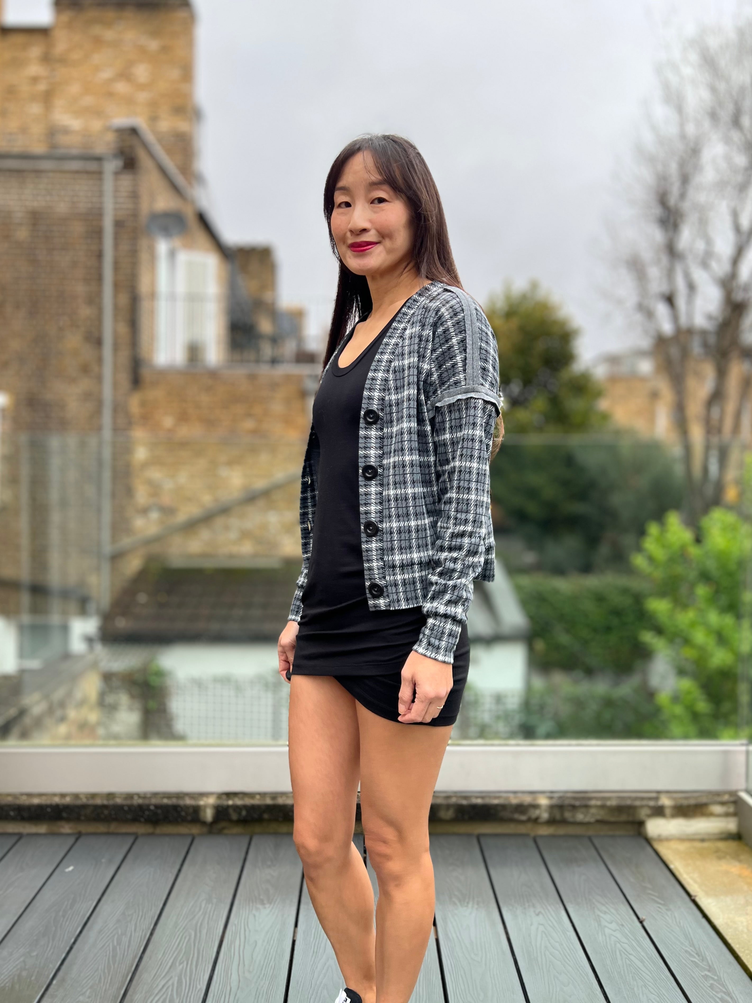 Woman standing on a rooftop with a blurred background wearing a plaid cropped cardigan sweater over a tulip dress.