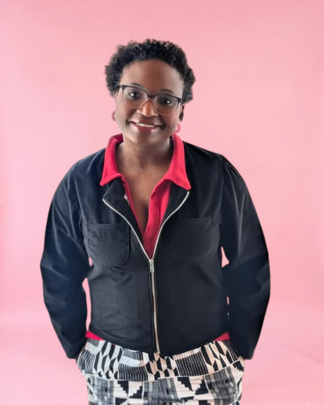 Person wearing a black jacket with a red shirt and patterned pants on a pink background. Easy woven jacket pattern.
