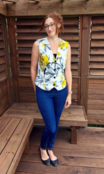 Woman wearing a floral vest with welt pockets and denim skinny jeans standing on a wooden deck.