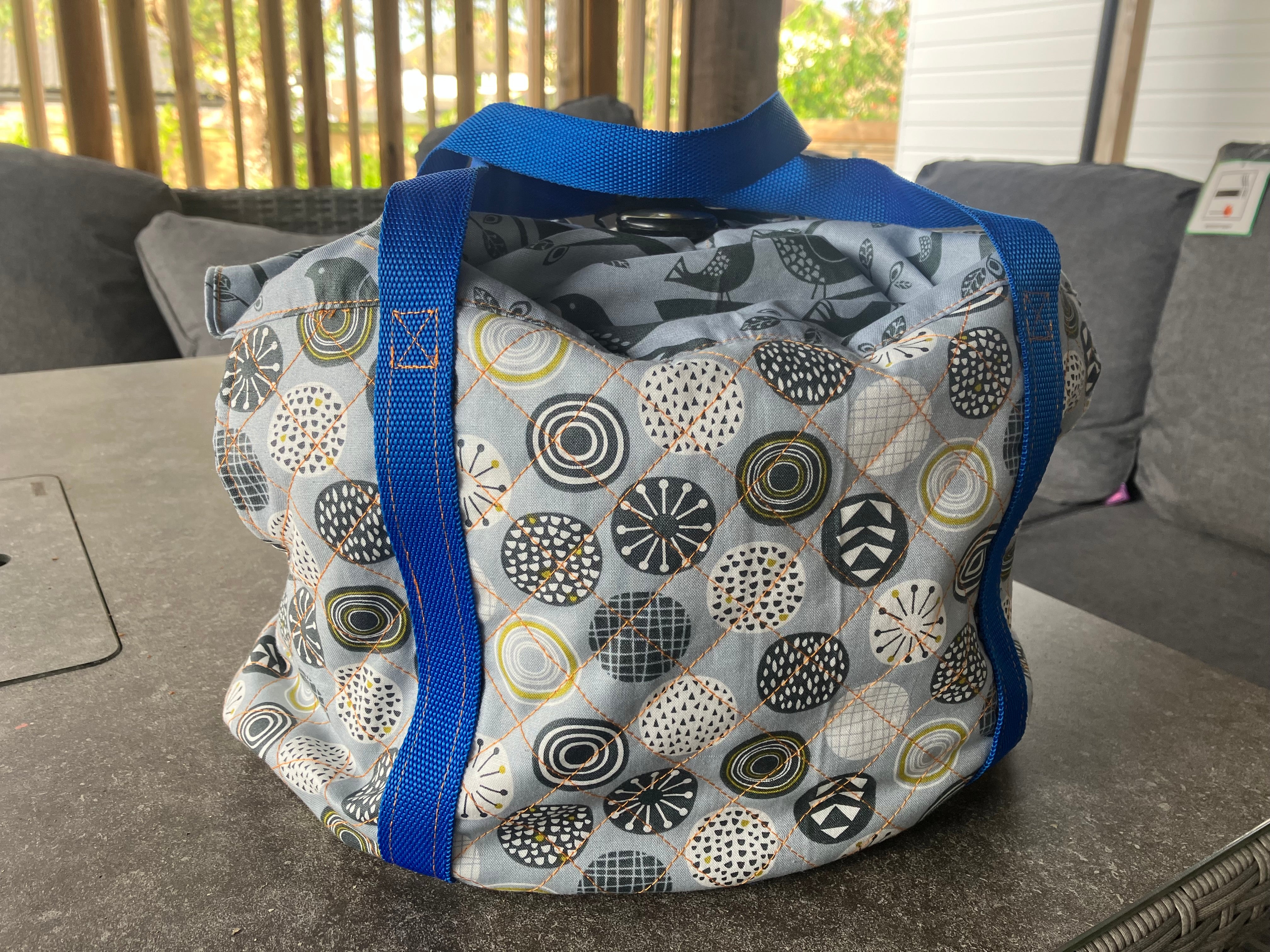 Patterned crock pot bag with blue straps on a table. Quilted sides and insulation make this the perfect slow cooker carrier for all your events! Easy to sew for beginners.