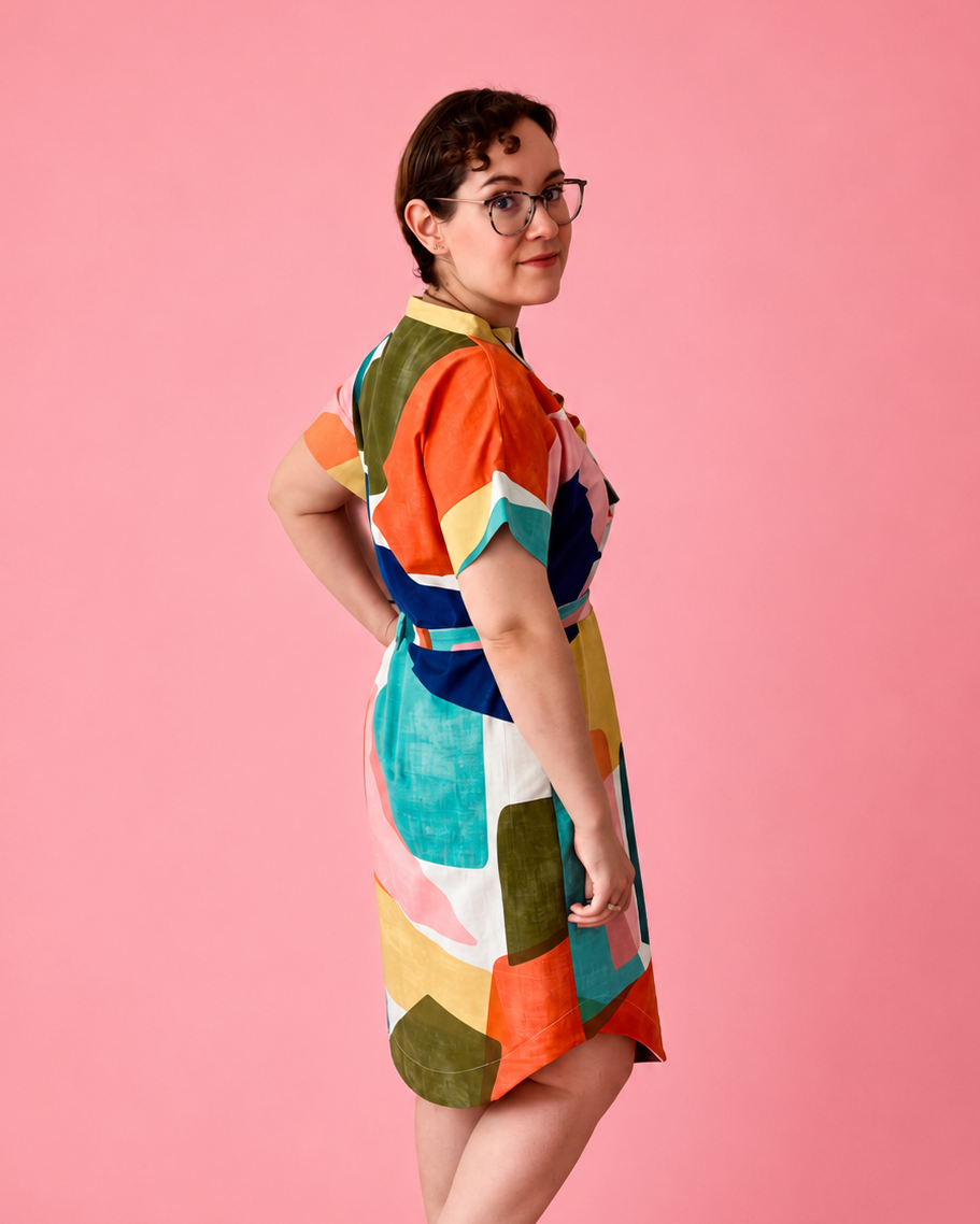 A woman wearing a colorful geometric print dress and teal high heels, posing in profile against a solid pink studio background. made using Ellie and Mac PDF sewing patterns. They include A0, A4, Letter, print files and projector sewing file. They also include a full sew along video tutorial.