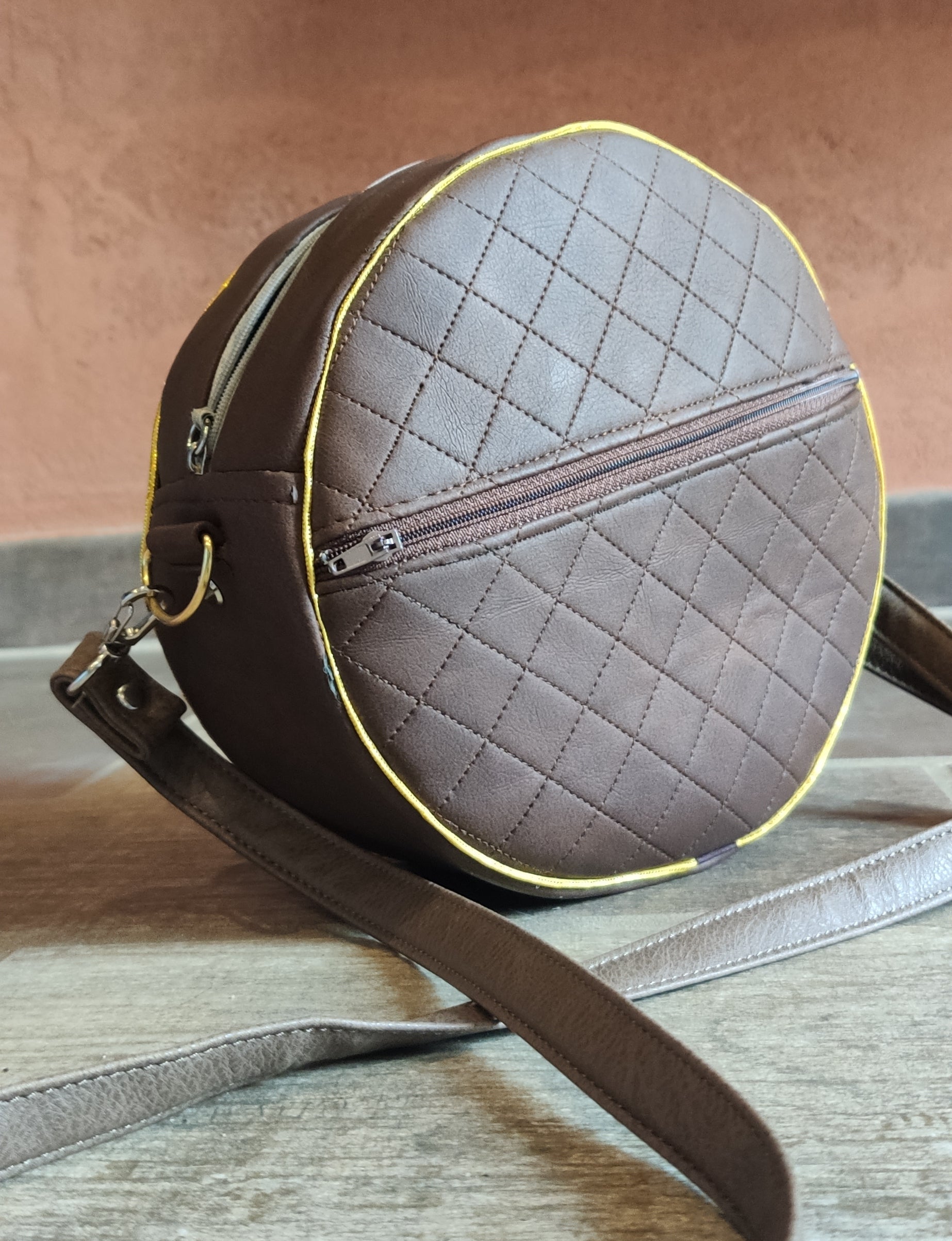 Round quilted leather bag with a strap on a wooden surface