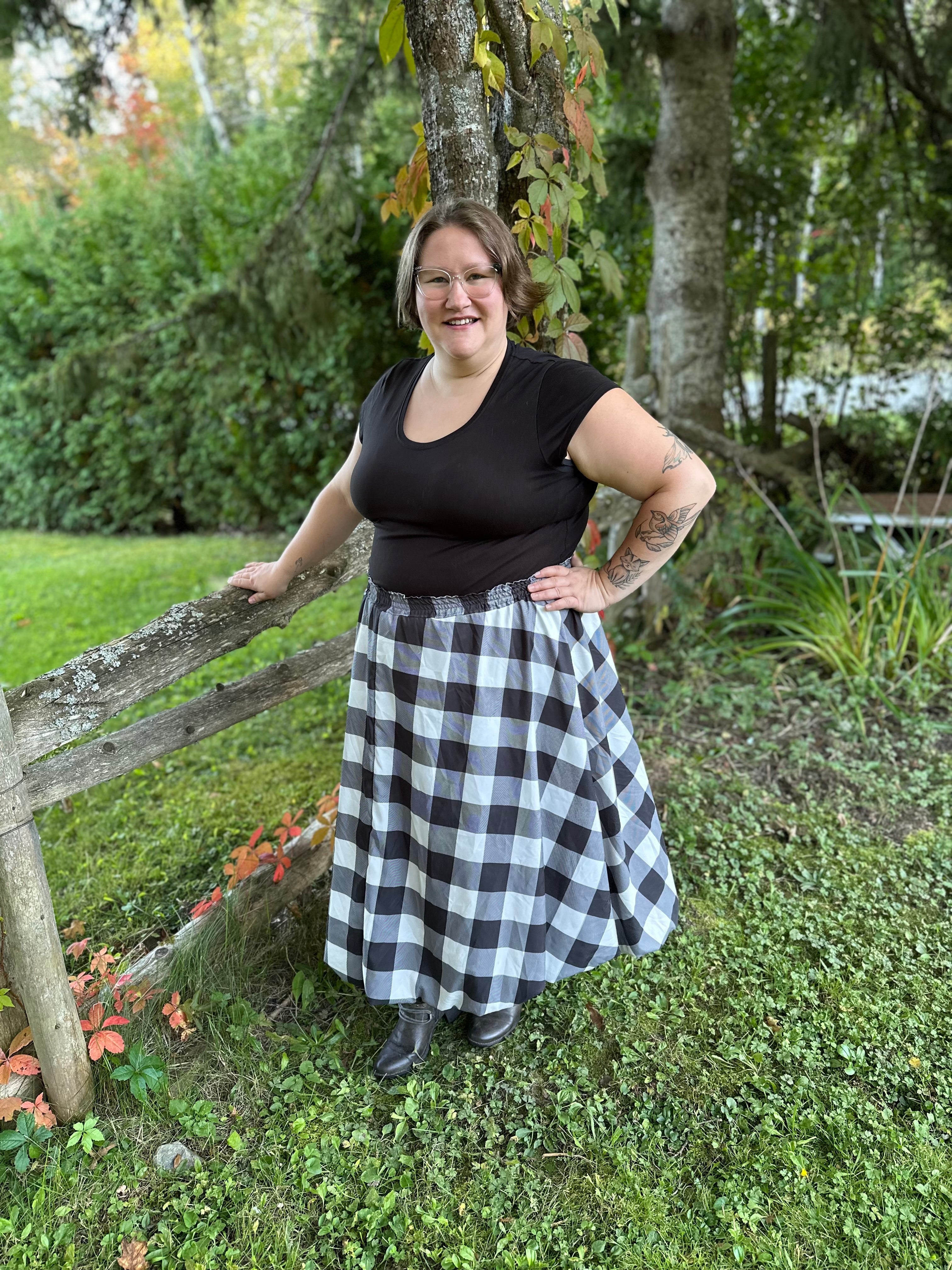 Person wearing a black top and checkered midi bubble skirt standing outdoors near a wooden fence.