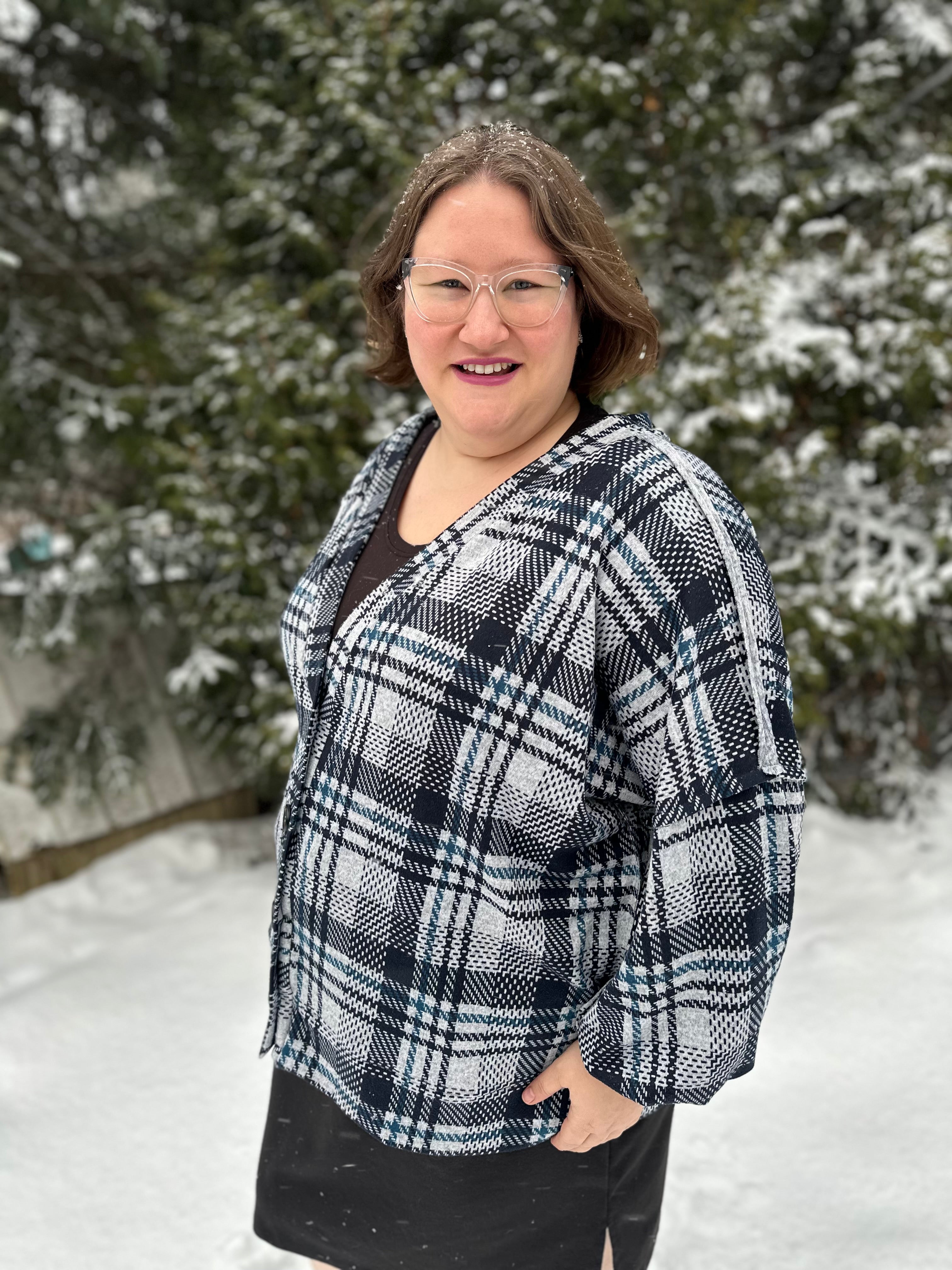 Person wearing a black and white plaid cardigan and black skirt in a snowy outdoor setting