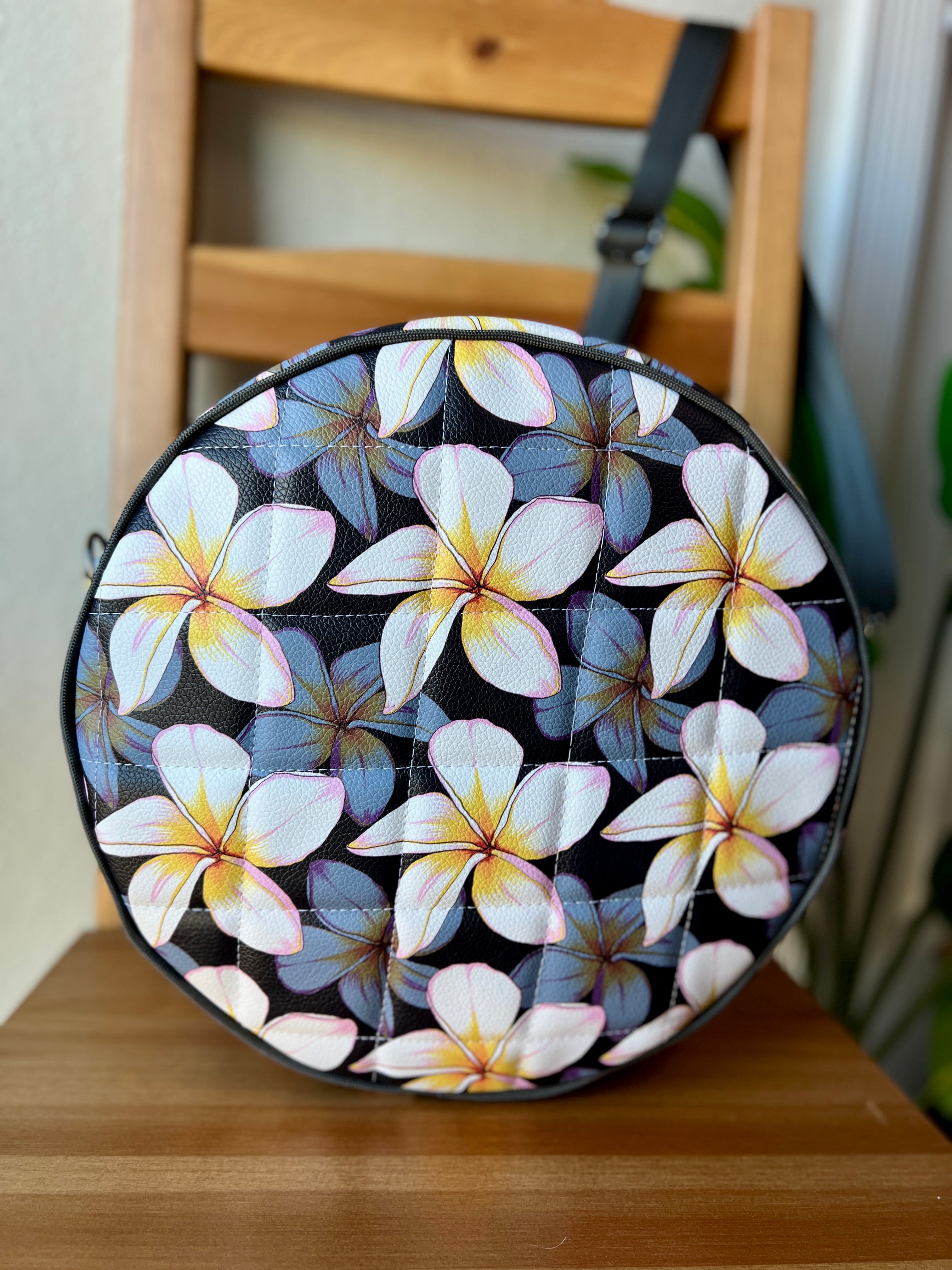 Handcrafted round vinyl bag in black floral vinyl with black hardware and hidden strap connectors.
