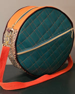 Teal handmade round bag with orange strap and leopard print accents on a dark surface.